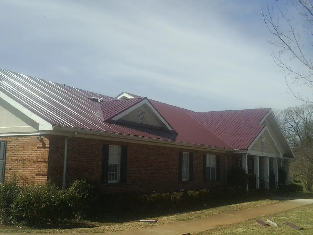 Red metal roof with gabled entries on a long brick building, from a Hail Damage Roof Repair job in Flagler Beach