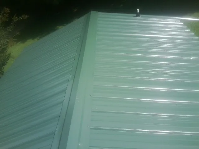 New green metal panels meeting at the ridge of a roof — Flat Roof Repair work by our crew in Flagler Beach