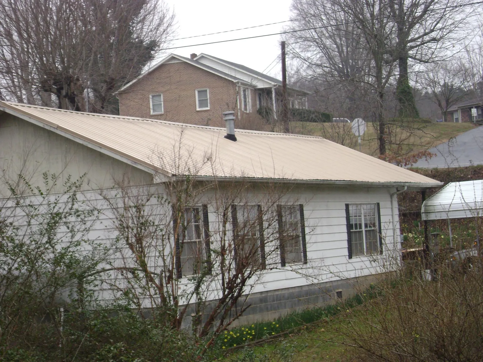 Tan metal roof on a white sided house set into a hillside — Commercial Roofing by Roofing Brothers in Flagler Beach